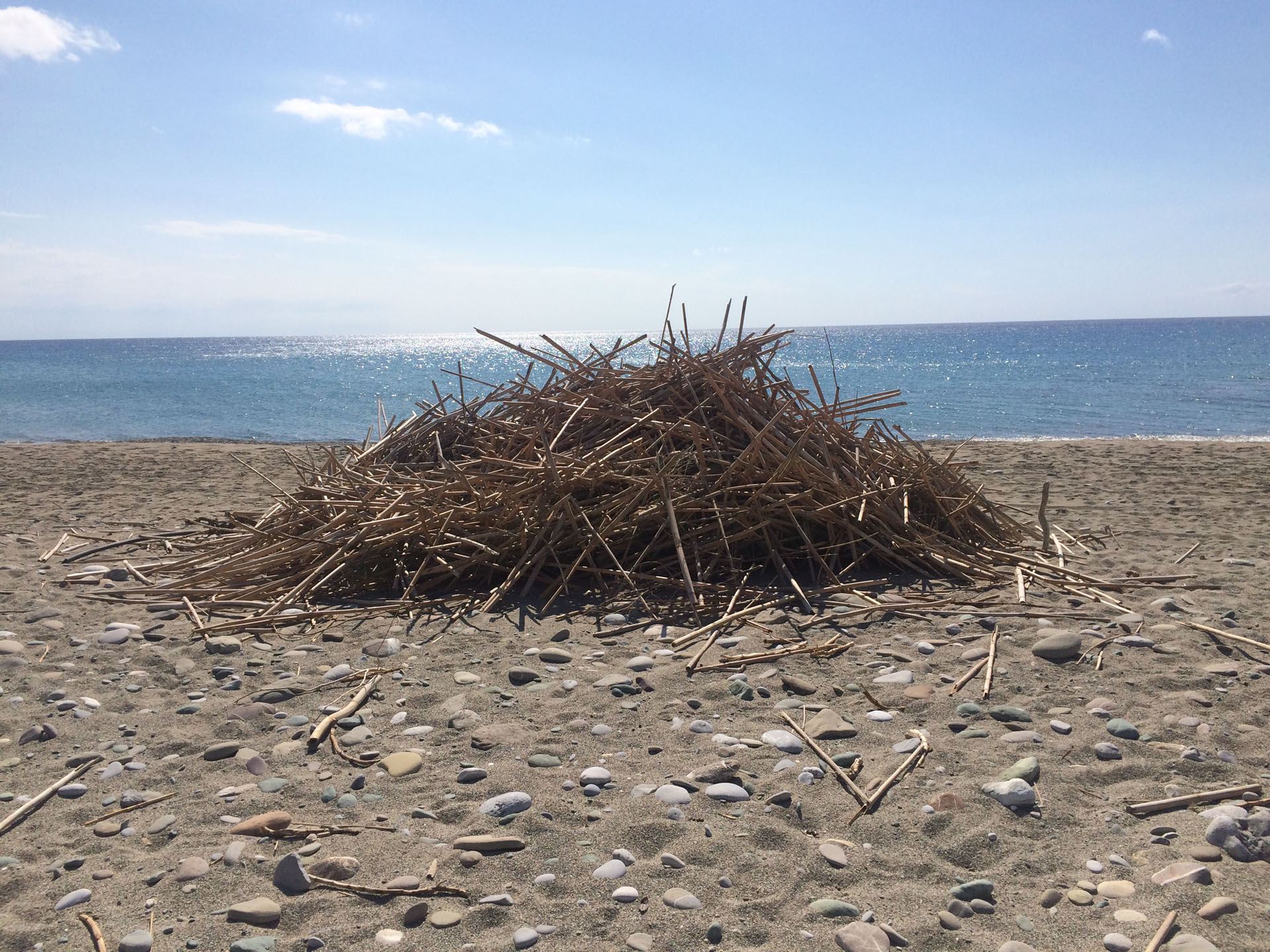 A cairn-type structure on a beach made from loads of dried out hollow sticks